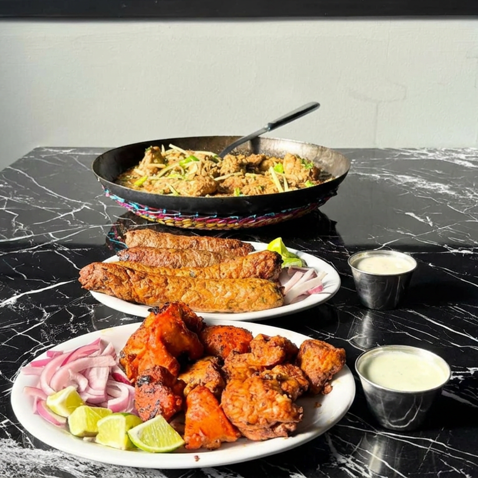 Indian appetizers, including fried chicken, pakoras, kebabs, chutney, lime wedges, and pickled onions, served on a marble table.